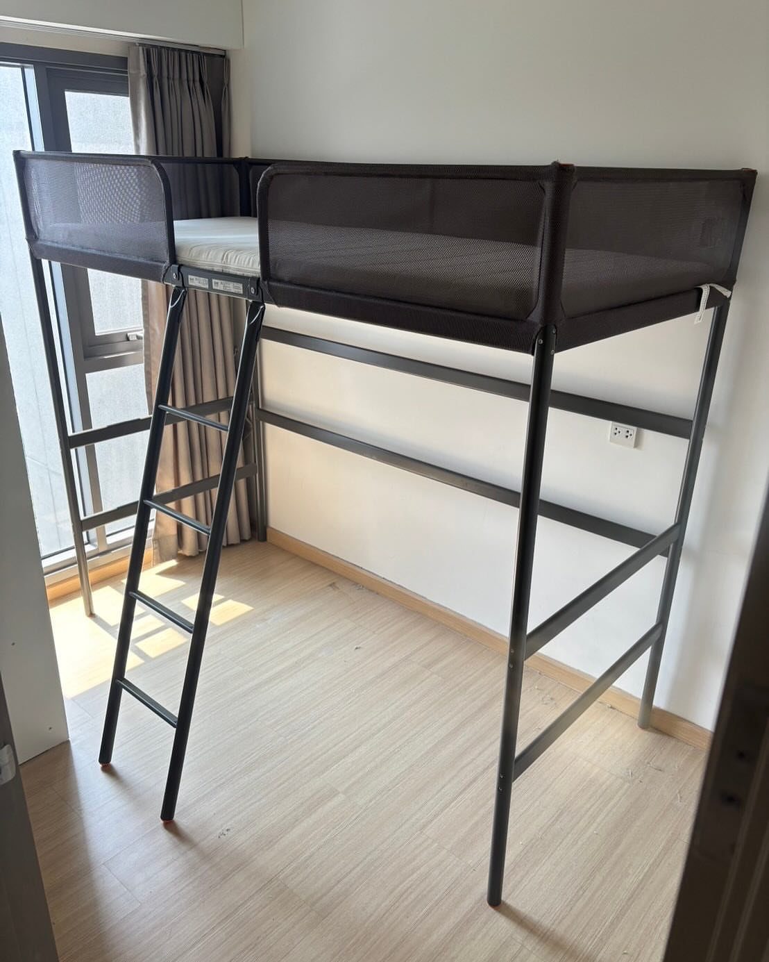 Black metal loft bed frame with ladder in a bright room with wood floors.