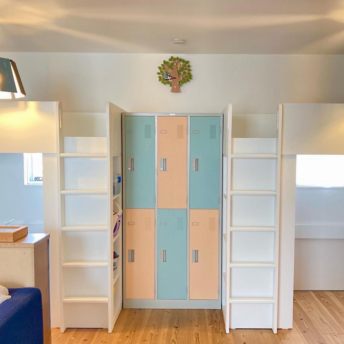 Two white loft beds flanking pastel blue and peach lockers in a bright room