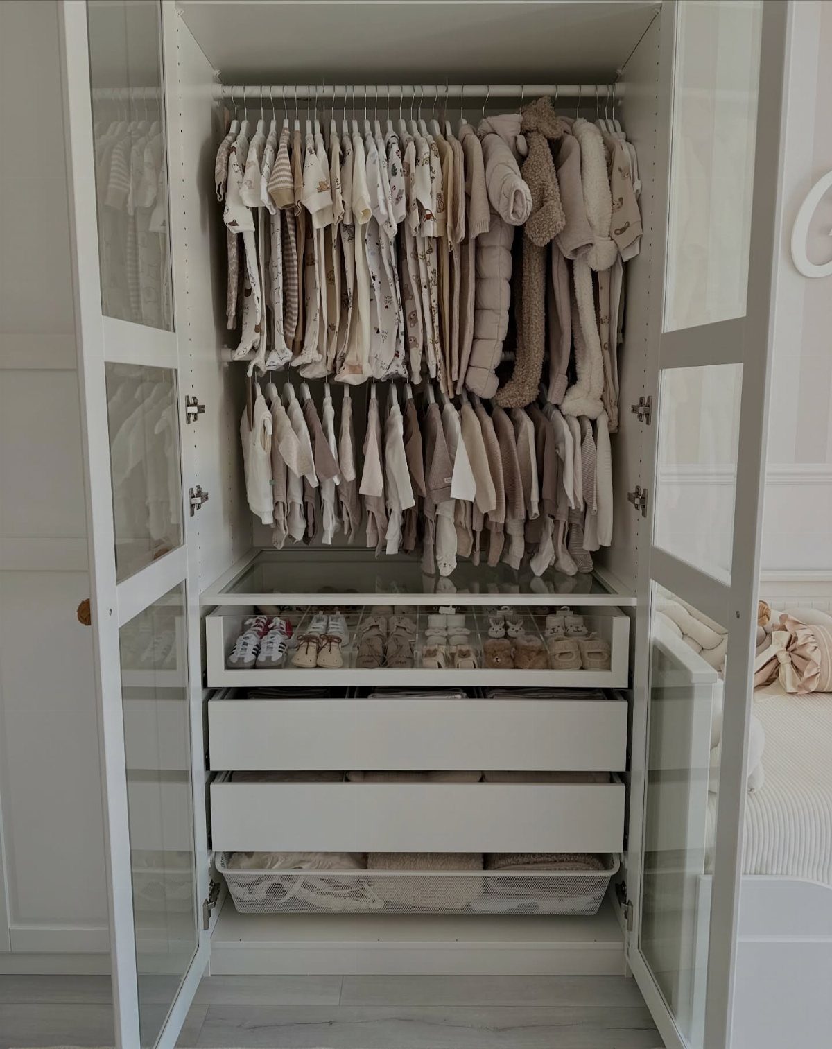 White nursery closet with organized neutral baby clothes and storage drawers.