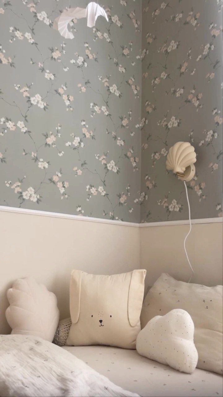 Sage green floral wallpaper above a white daybed with cream plush pillows.