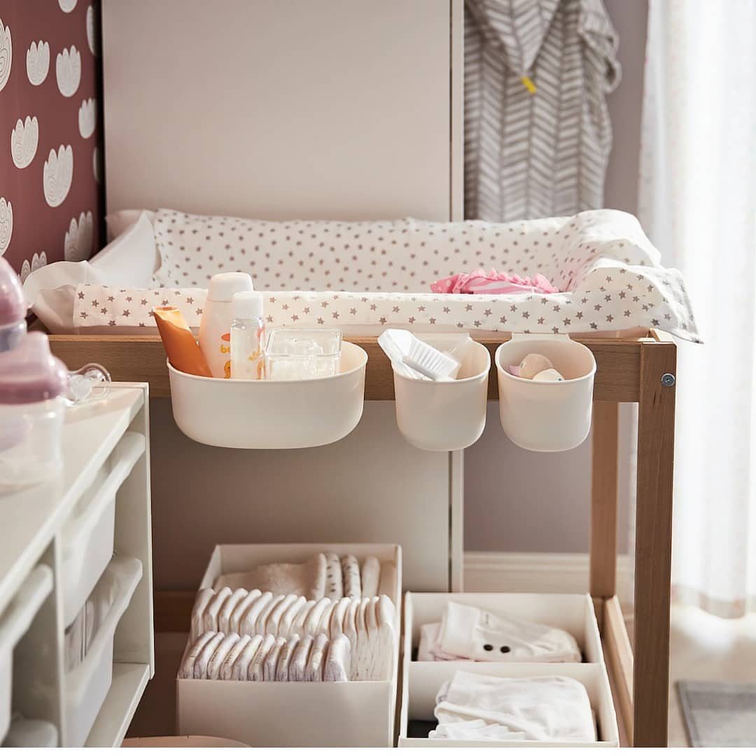 Wooden baby changing table with hanging storage bins and organized clothes underneath.