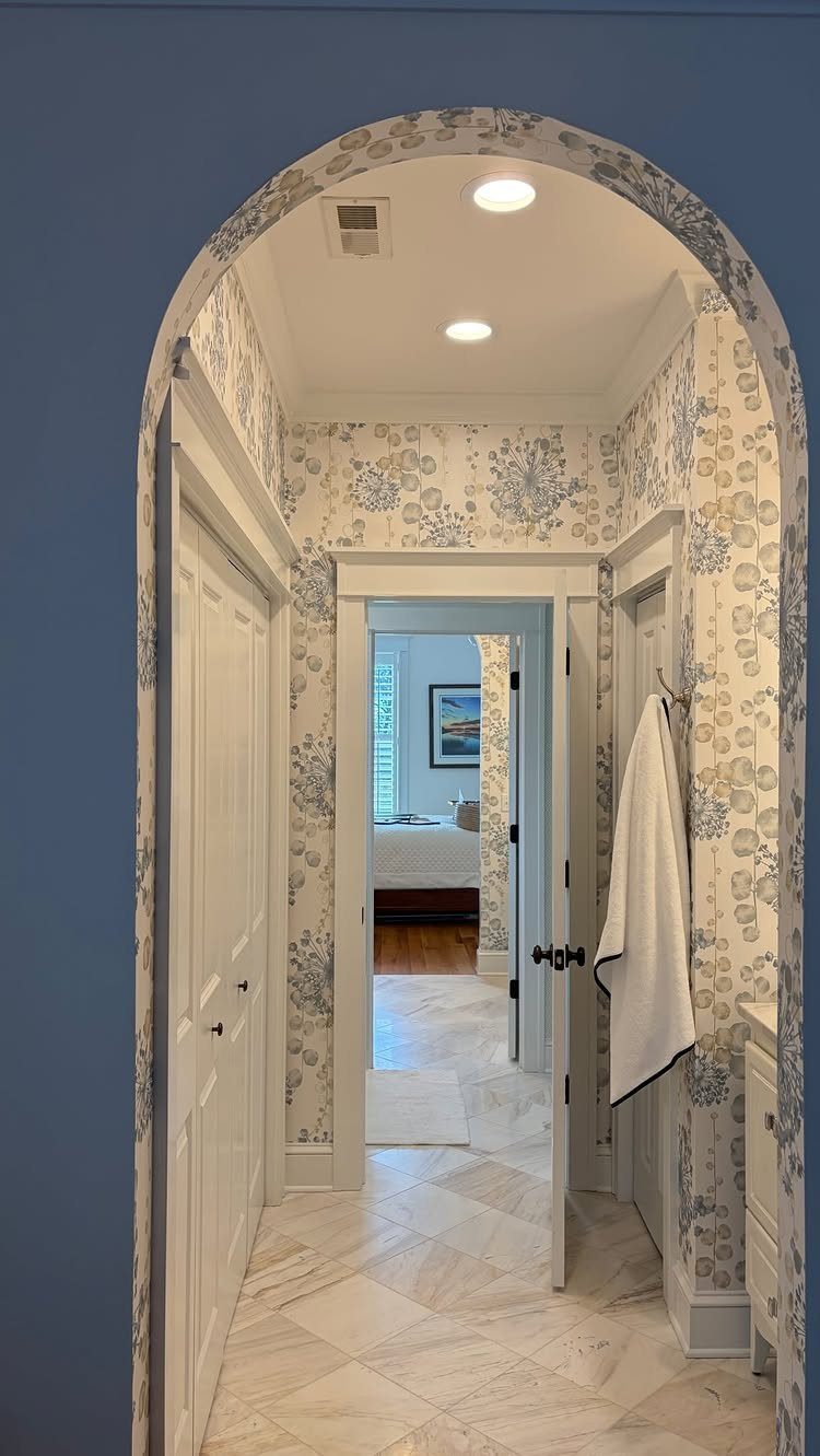 Bathroom hallway with floral wallpaper and two white doors providing dual access.