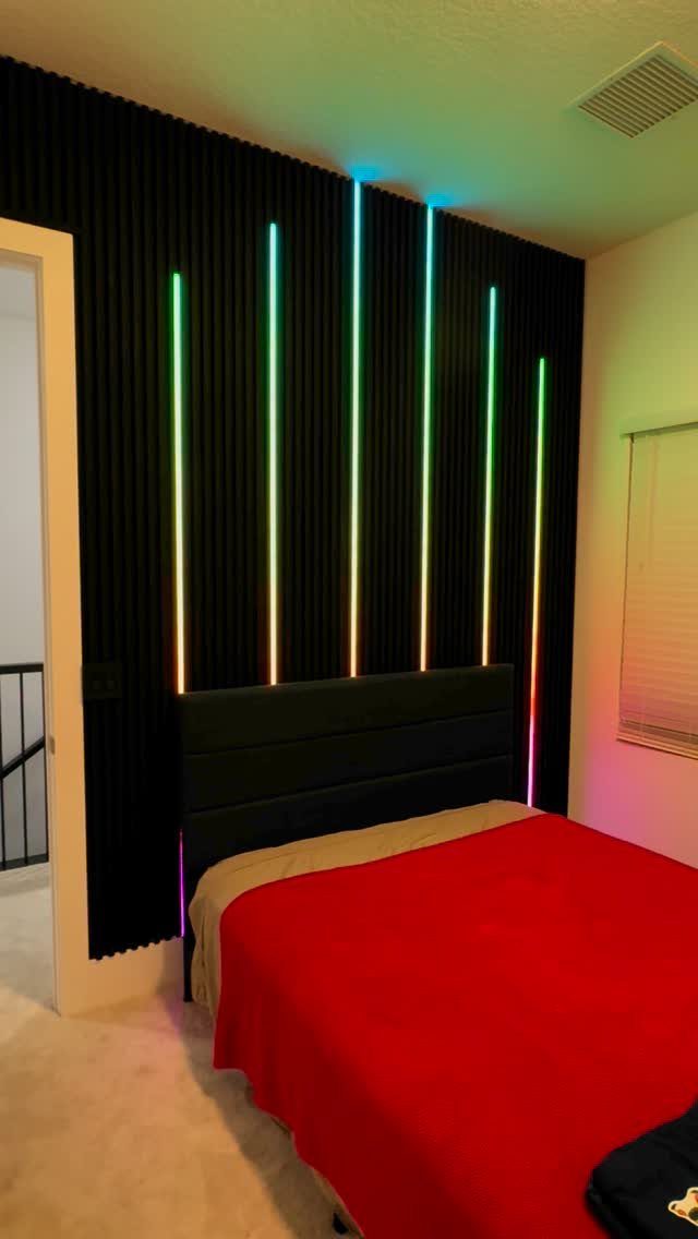 Black slatted accent wall with vertical colorful LED light strips behind a bed.