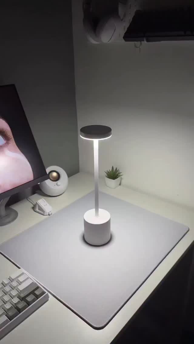 Modern white cylindrical desk lamp illuminating a grey desk mat and workspace.