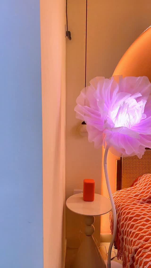 Purple flower-shaped floor lamp illuminating a bedroom corner with orange bedding