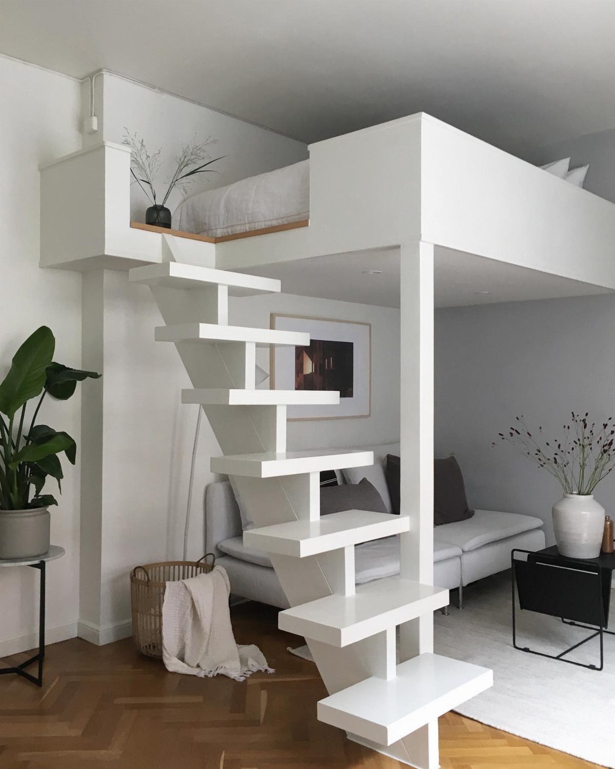 White loft bed with stairs over a living area with a grey sofa.