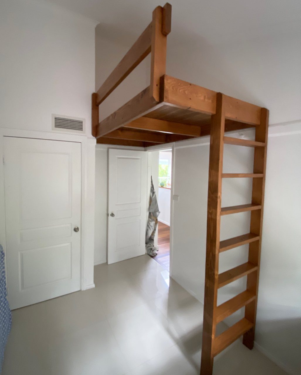 Wooden loft bed frame with integrated ladder in a bright white room.