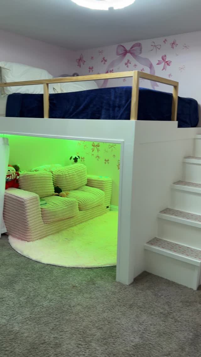 White wooden loft bed with stairs and a cozy lounge area underneath.