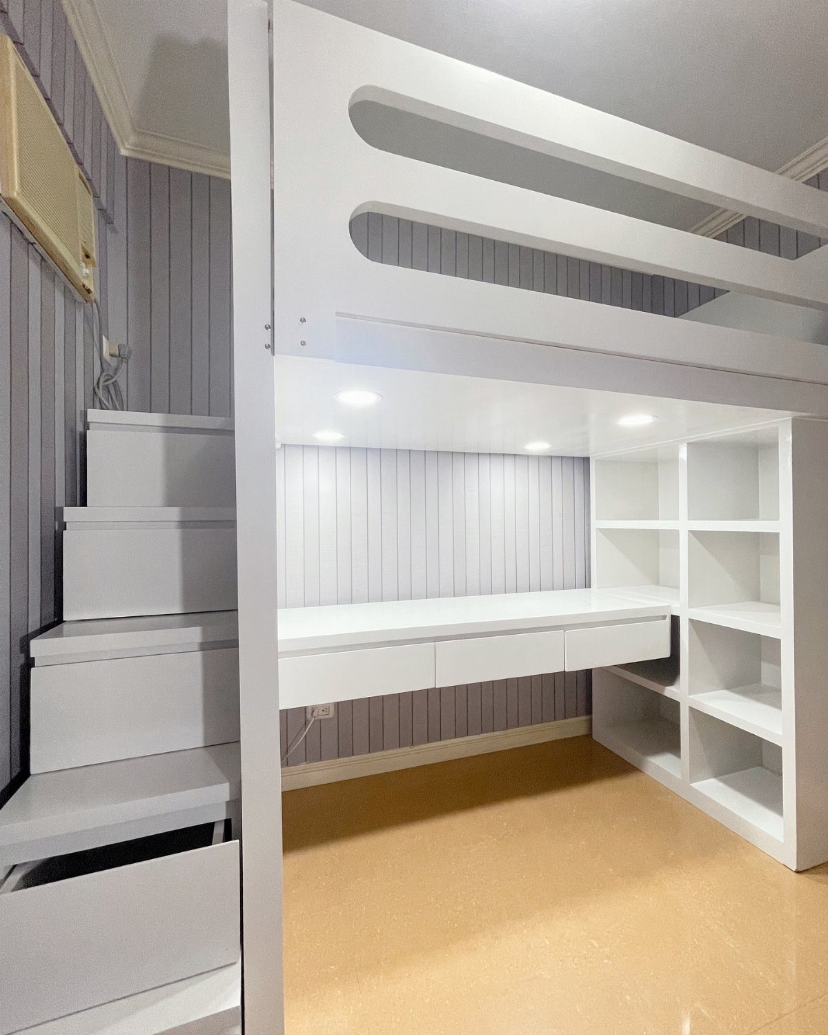 White painted loft bed with integrated desk, shelves, and storage stairs against purple walls.