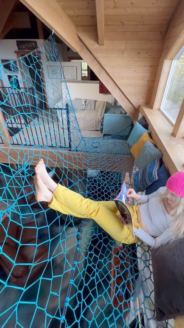 Woman relaxing in a blue rope net hammock under a wooden loft bed