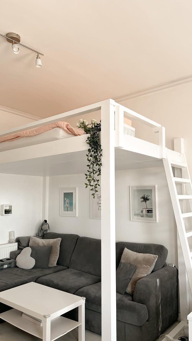 White loft bed with a grey sectional sofa and coffee table underneath.