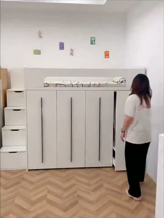White loft bed with large storage cabinets underneath and a woman standing beside.