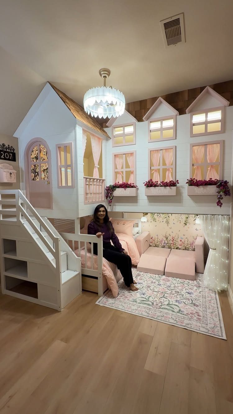 White house-shaped loft bed with pink accents and a cozy seating area below.