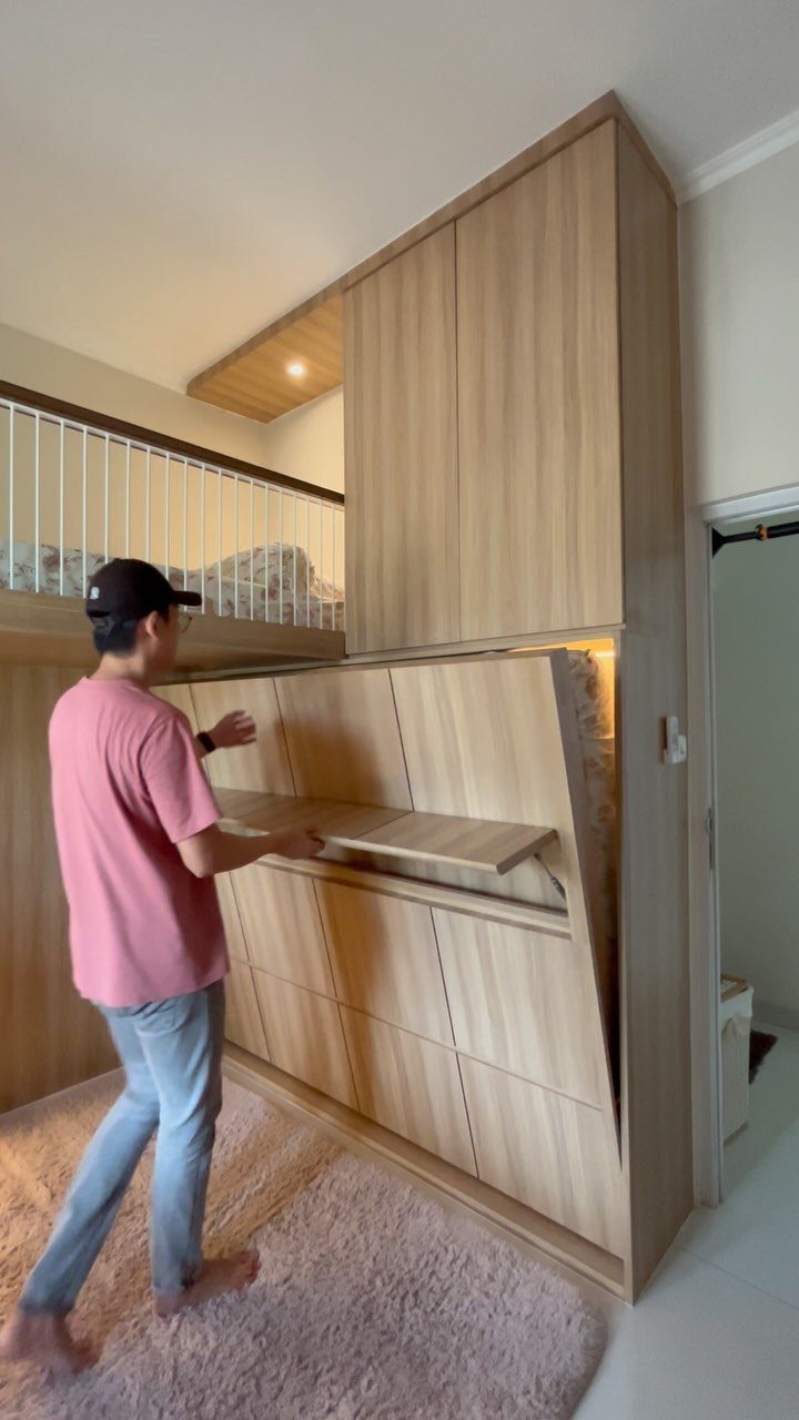 Man opening a hidden desk compartment beneath a wooden loft bed in a bedroom