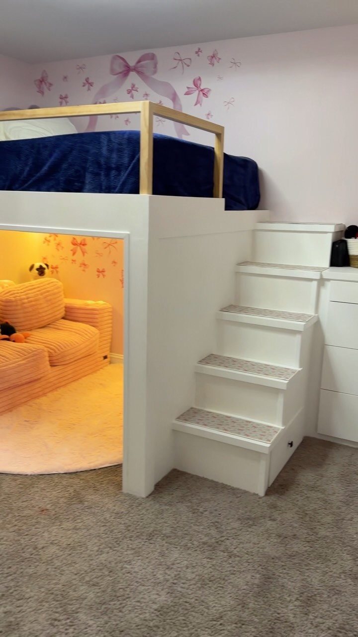 White loft bed with a cozy pink sofa and rug in the play area below.