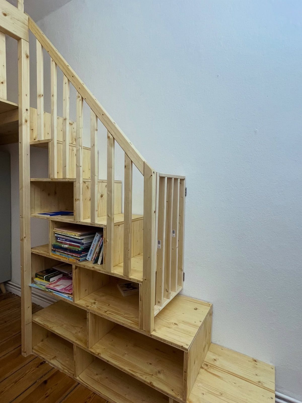 Wooden loft stairs with built-in bookshelves and a small secret door access point.