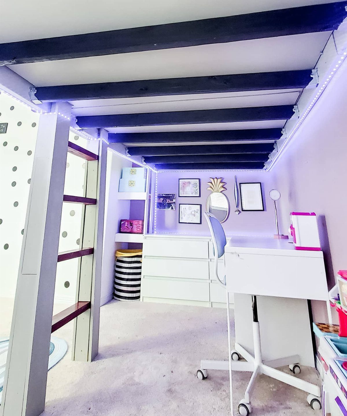Loft bed with a white desk and purple LED lighting underneath in a studio.