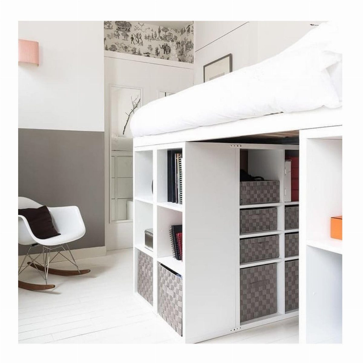 White loft bed with built-in storage shelves and a white rocking chair nearby.