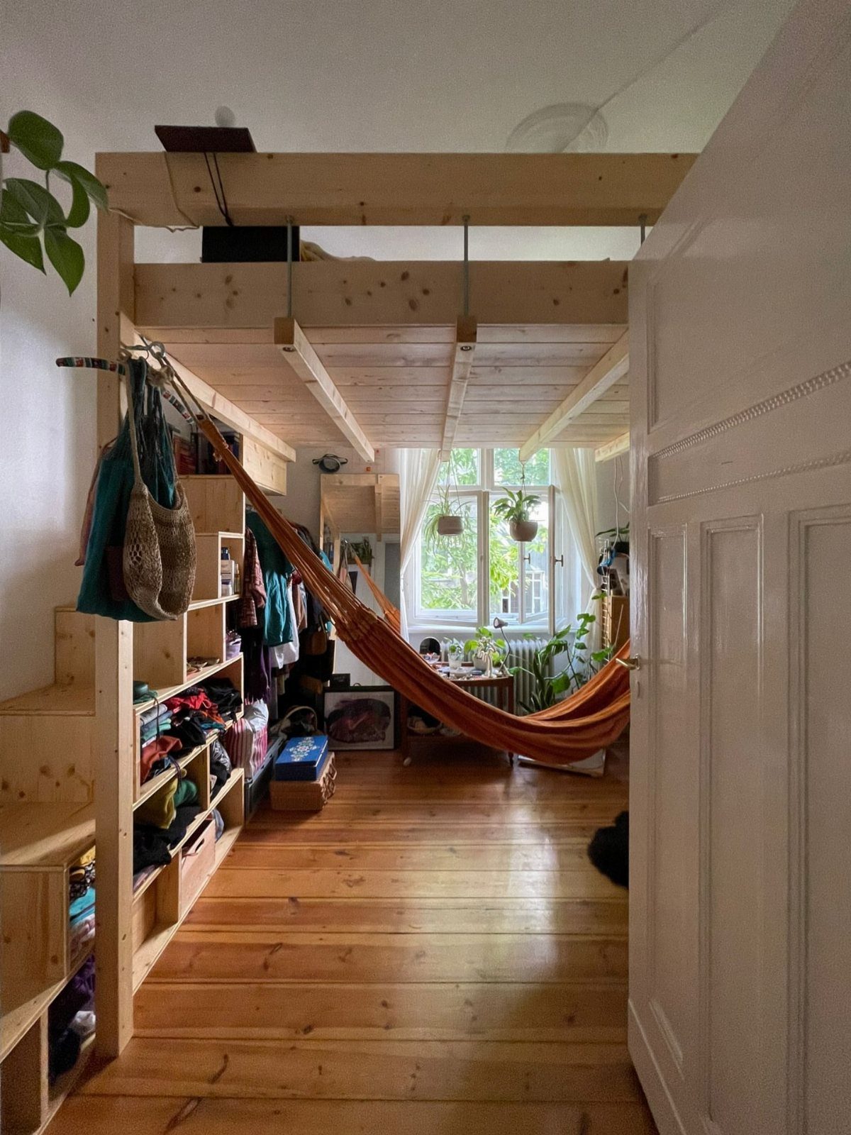 Wooden loft bed with built-in shelving and an orange hammock underneath in a room.