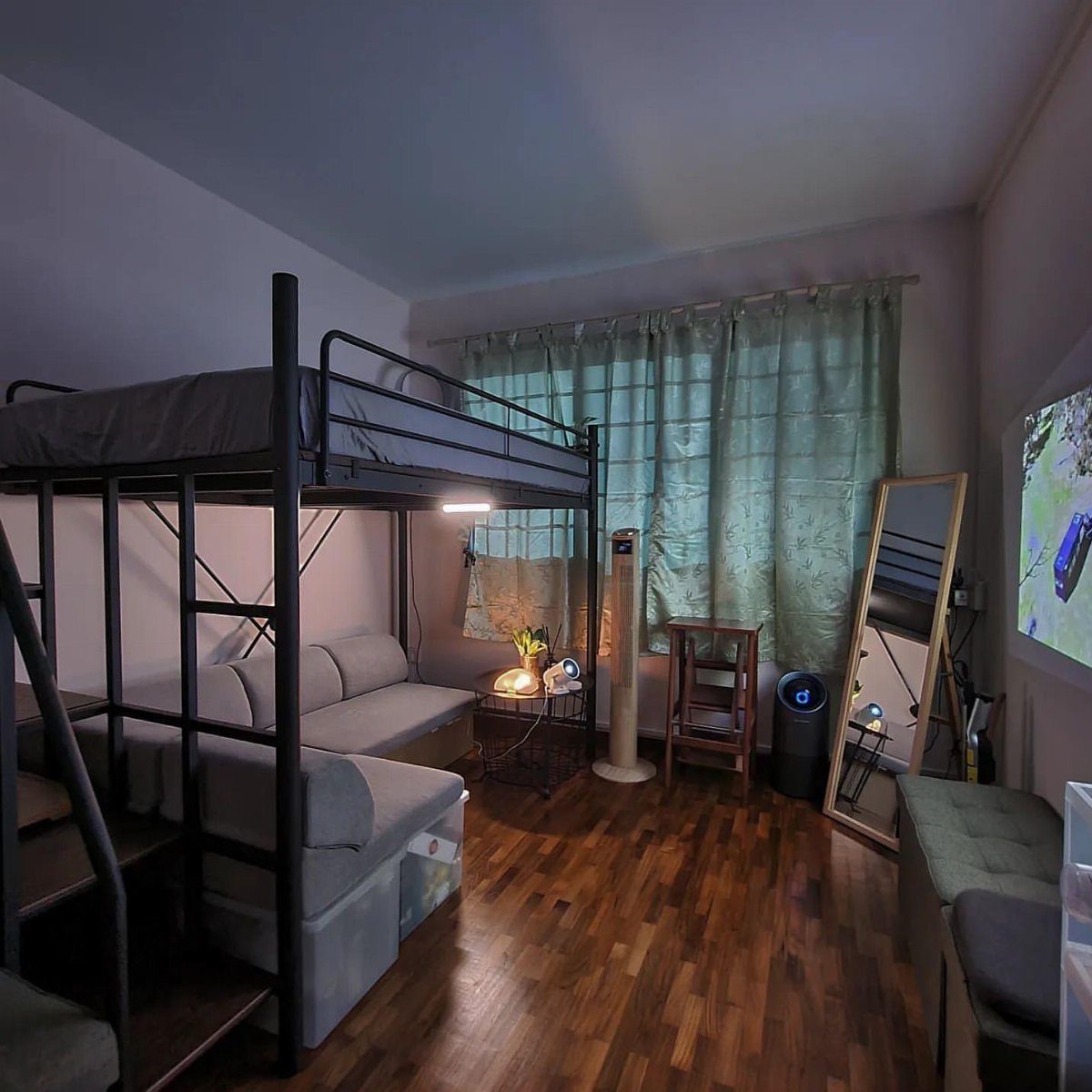Black metal loft bed with a grey sofa placed underneath in a bedroom.