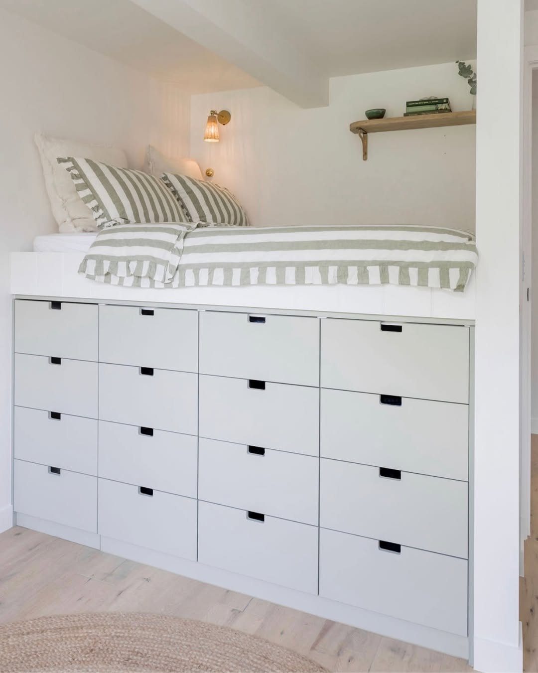 White loft bed with striped bedding and integrated storage drawers underneath in a room.