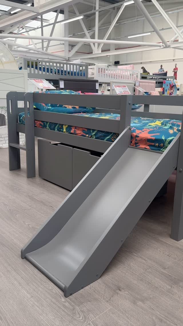 Grey wooden loft bed with a slide and storage drawers in a showroom