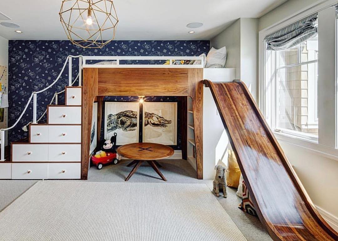 Wooden mid-loft bed featuring a polished slide and integrated storage stairs in a bedroom.