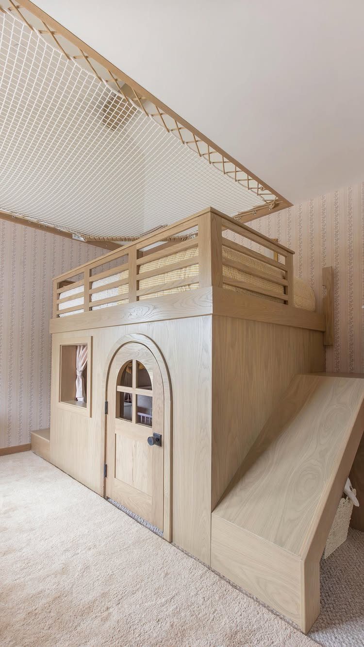 Wooden loft bed with a built-in playhouse and a slide in a bedroom.