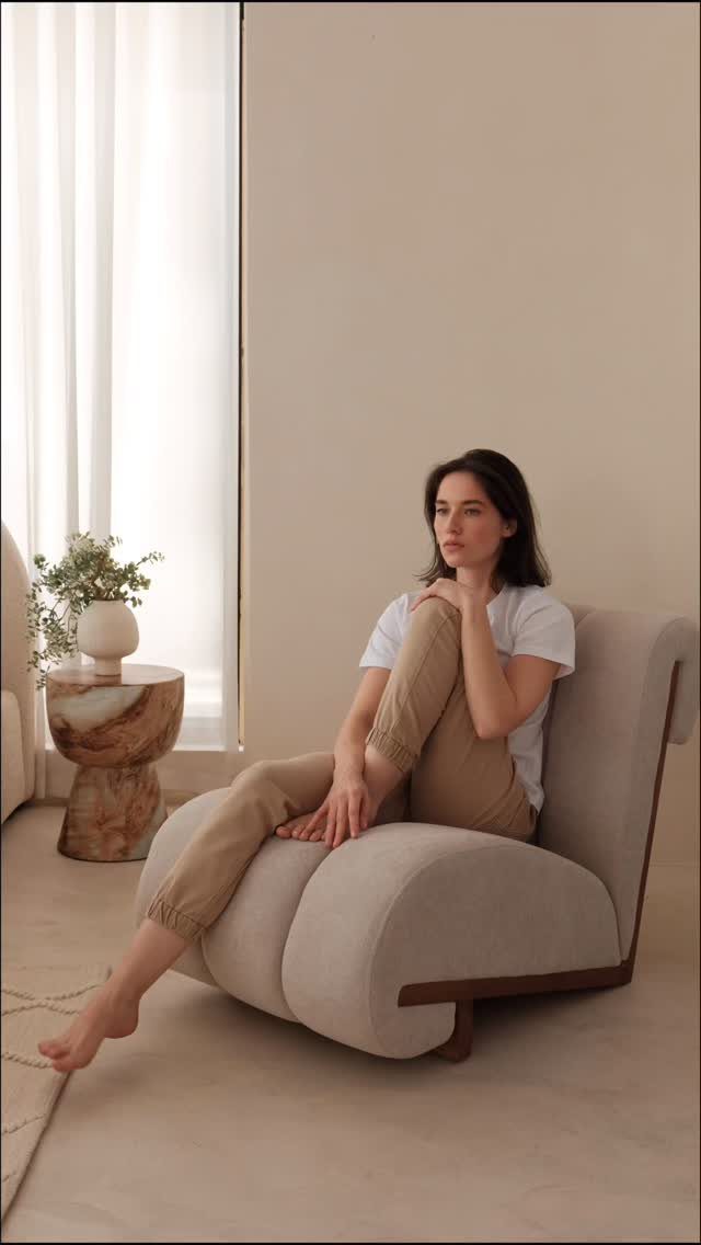Woman sitting in a curved beige armless lounge chair in a minimalist room.