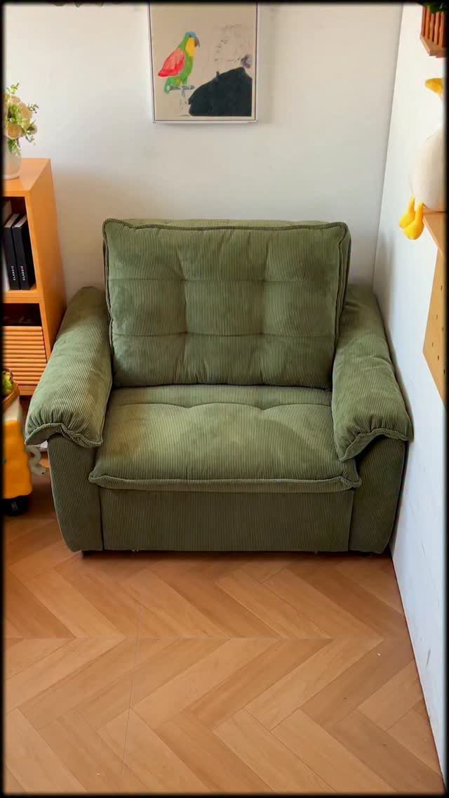 Green corduroy armchair with thick cushions on a herringbone wood floor.