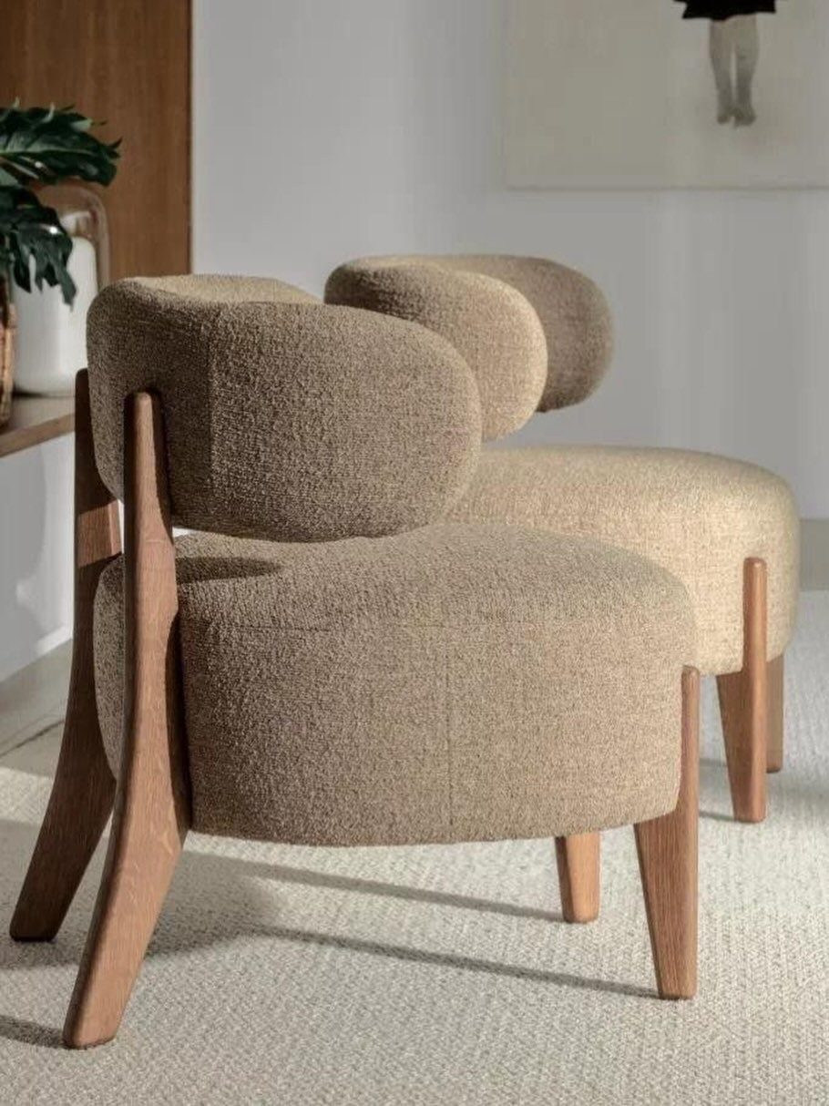 Beige bouclé lounge chairs with wooden frames in a bright, minimalist room.