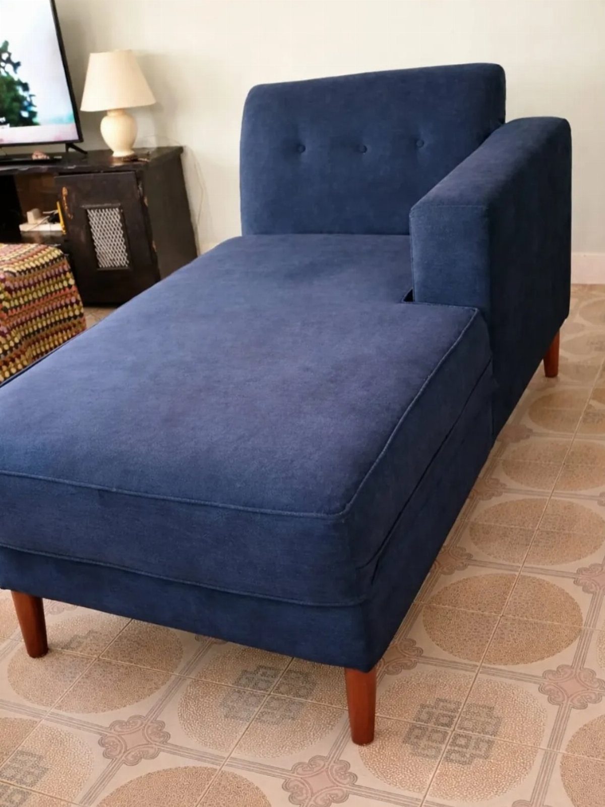 Navy blue chaise lounge chair with wooden legs on a patterned tile floor.