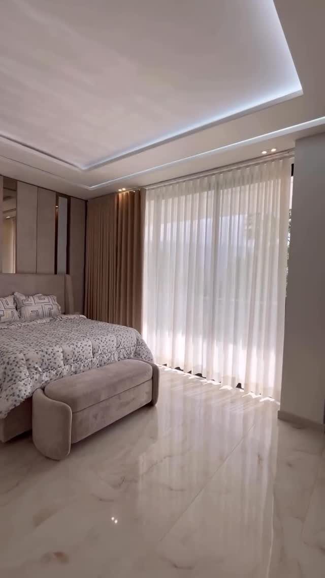 Floor-to-ceiling white and beige curtains in a modern luxury bedroom with marble floors.