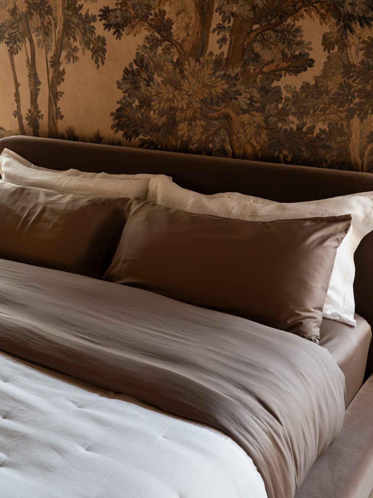 Brown and white bedding on a bed with forest landscape wallpaper background