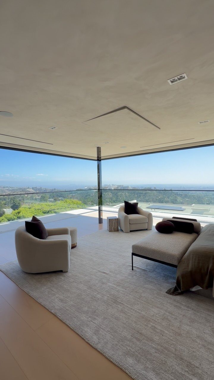 Modern luxury bedroom with cream armchairs and chaise lounge overlooking a scenic vista.