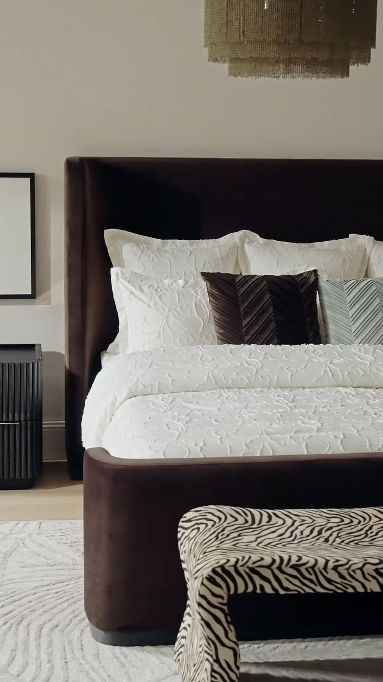 Dark brown velvet bed with white textured bedding and a zebra-print bench.