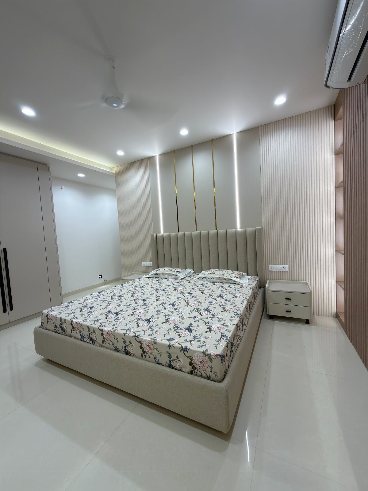 Modern bedroom with a beige channeled headboard, floral bedding, and illuminated wall paneling.