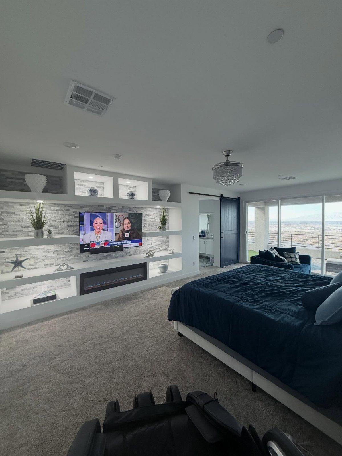 Modern bedroom with blue bedding, white feature wall, and a small corner seating area.