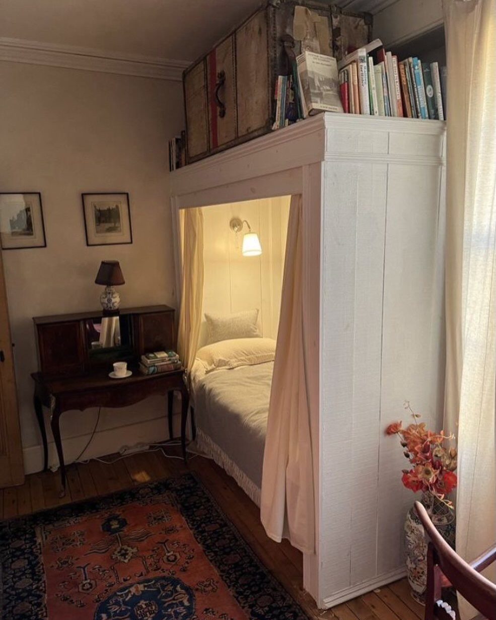 White wooden loft bed with curtains, books on top, and a vintage rug.