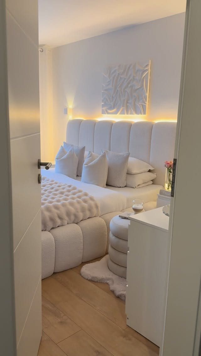 Modern white bedroom with warm backlight behind the ribbed headboard and wall art.
