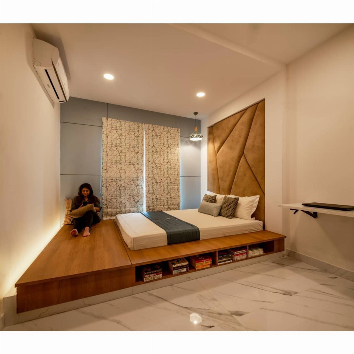 Wooden platform bed with a person sitting on the extended seating area nook.
