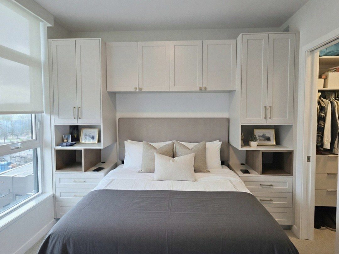 Symmetrical white built-in wardrobes and cabinets surrounding a bed with grey bedding.
