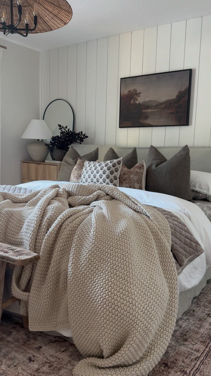 Bedroom with beige knit throw, white paneled wall, and woven light fixture.