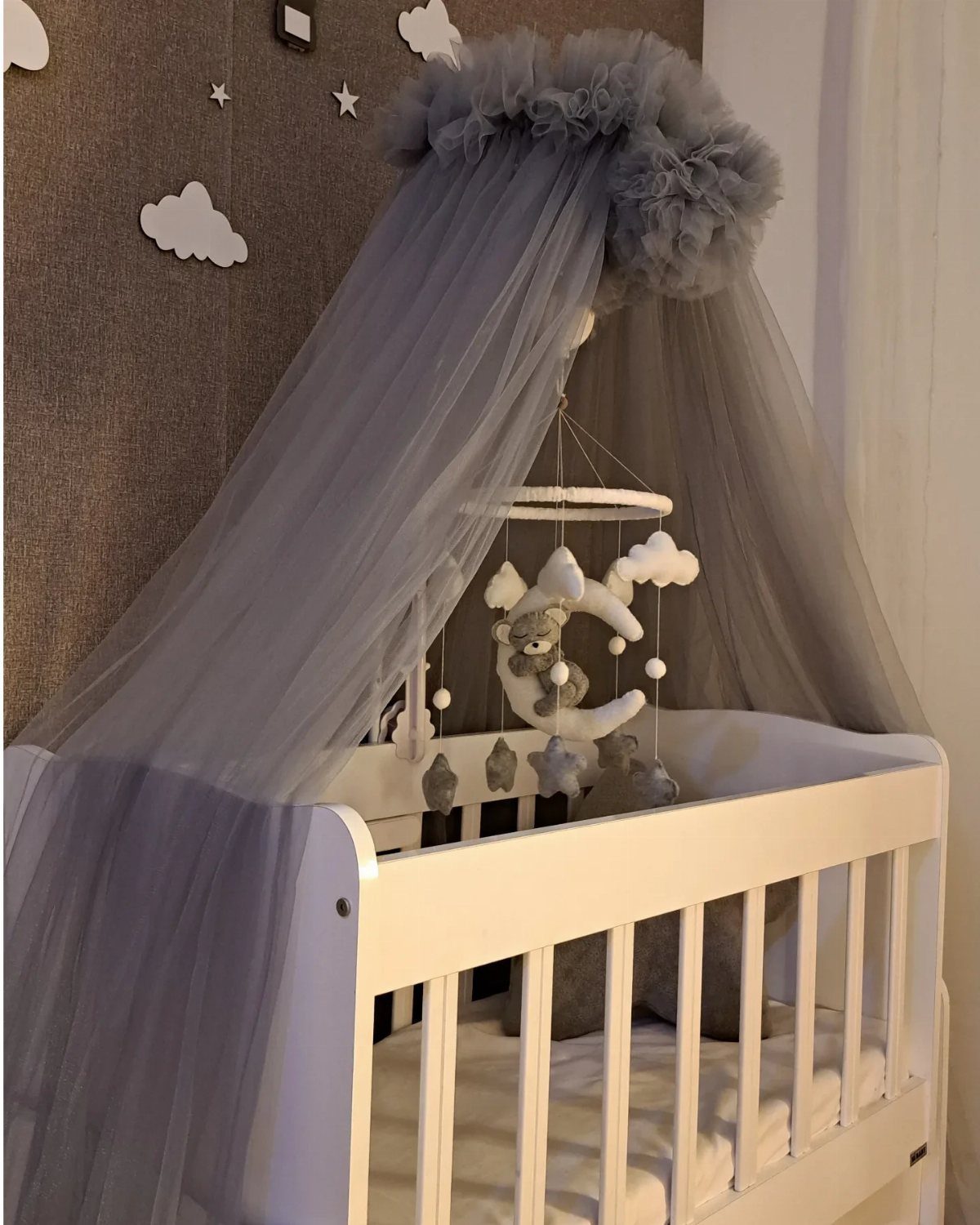 White mini crib with a grey tulle canopy and cloud wall decorations.