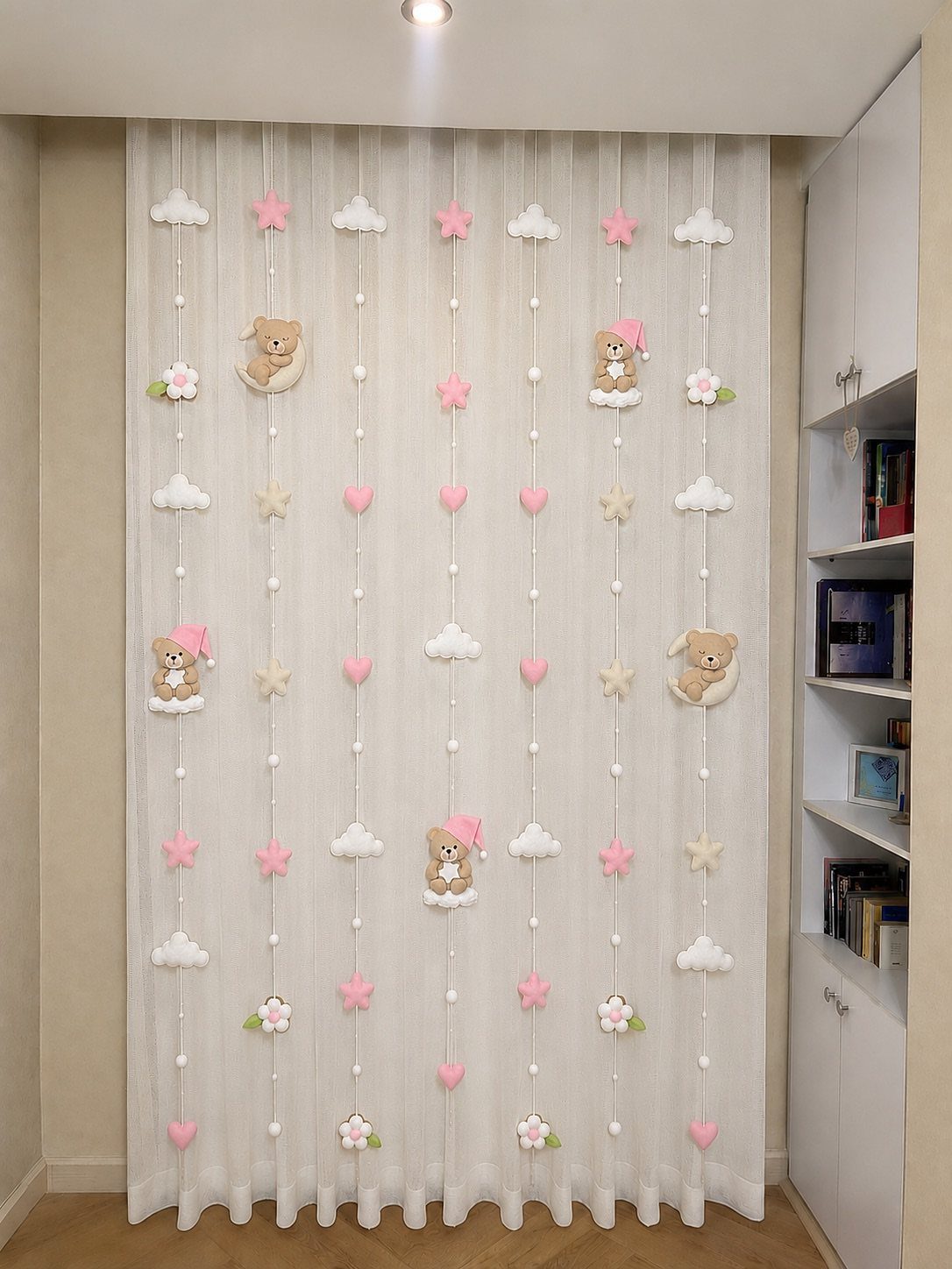 White sheer curtain decorated with plush teddy bears and pink ornaments in a nursery.