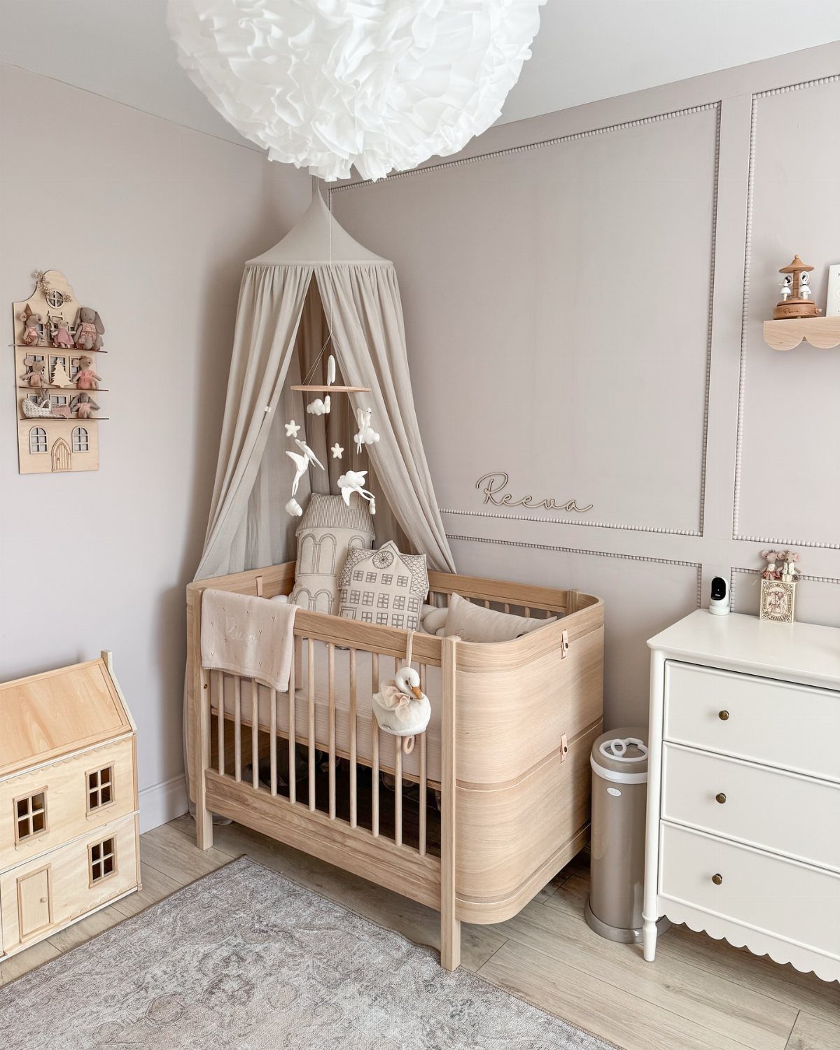 Wooden mini crib with a beige canopy tucked into a neutral nursery corner.