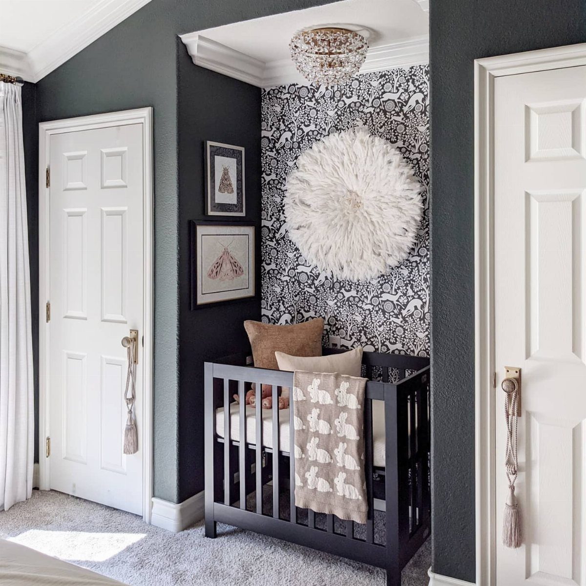 Black mini crib in a grey nursery nook with patterned wallpaper and wall art