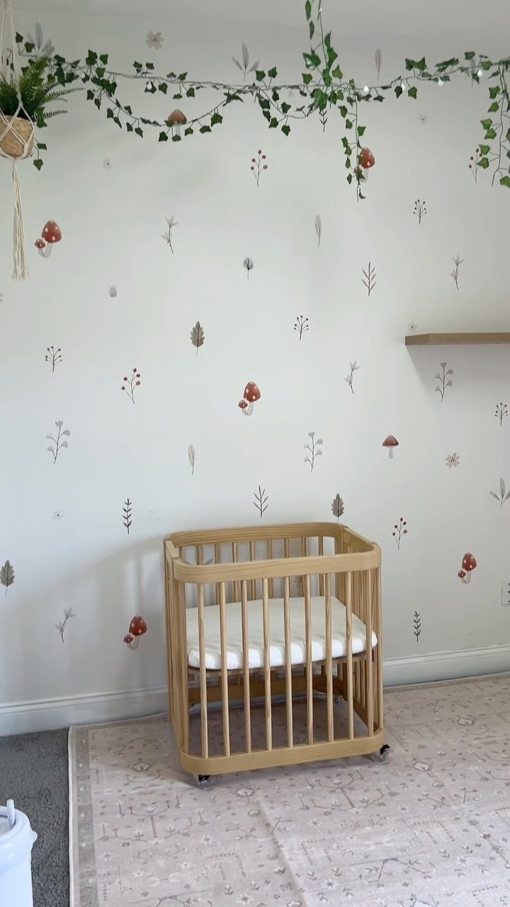 Wooden mini crib with white bedding against a floral patterned wall and ivy garland