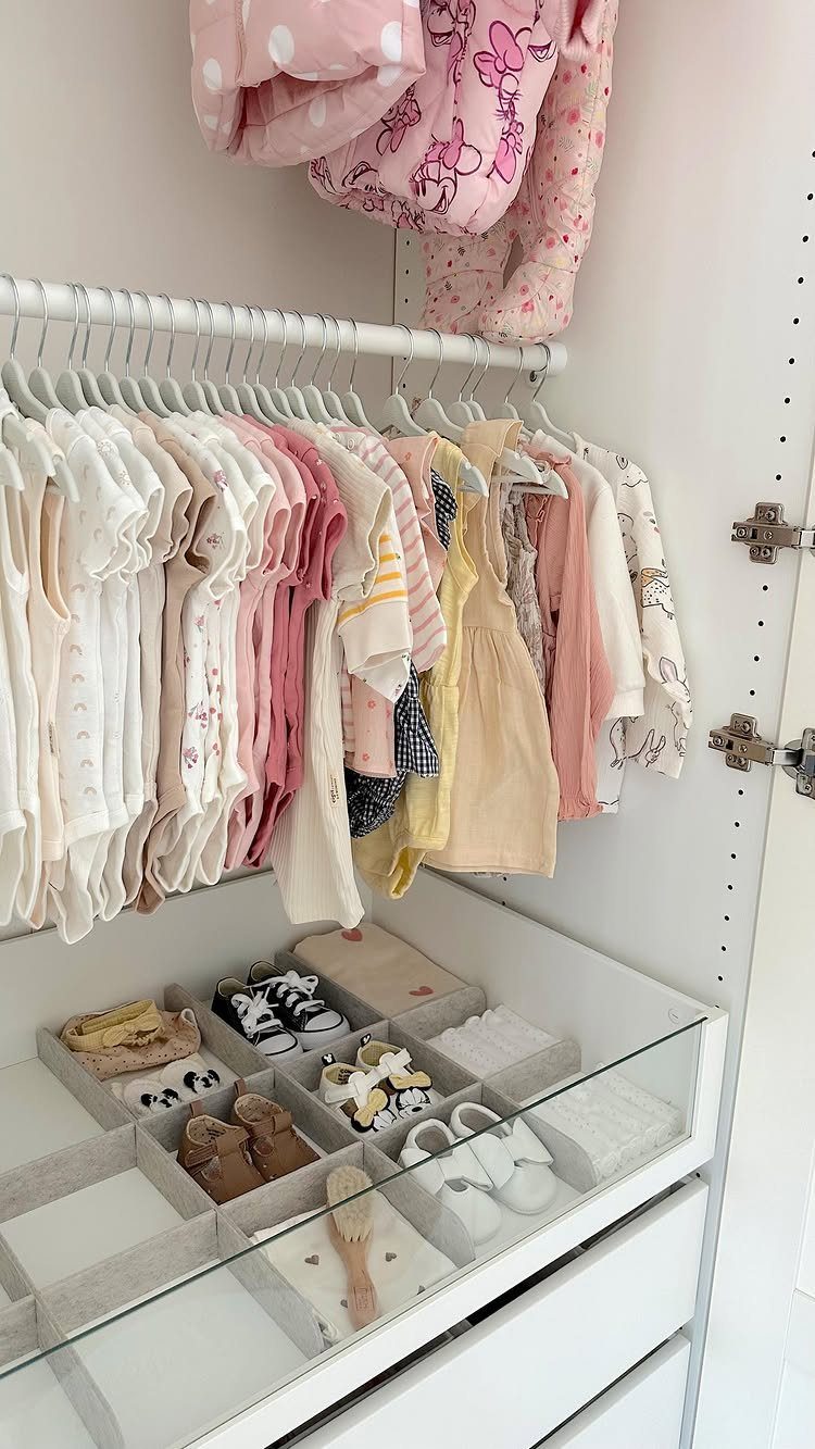 Open white baby closet with hanging pink clothes and organized shoes in dividers.