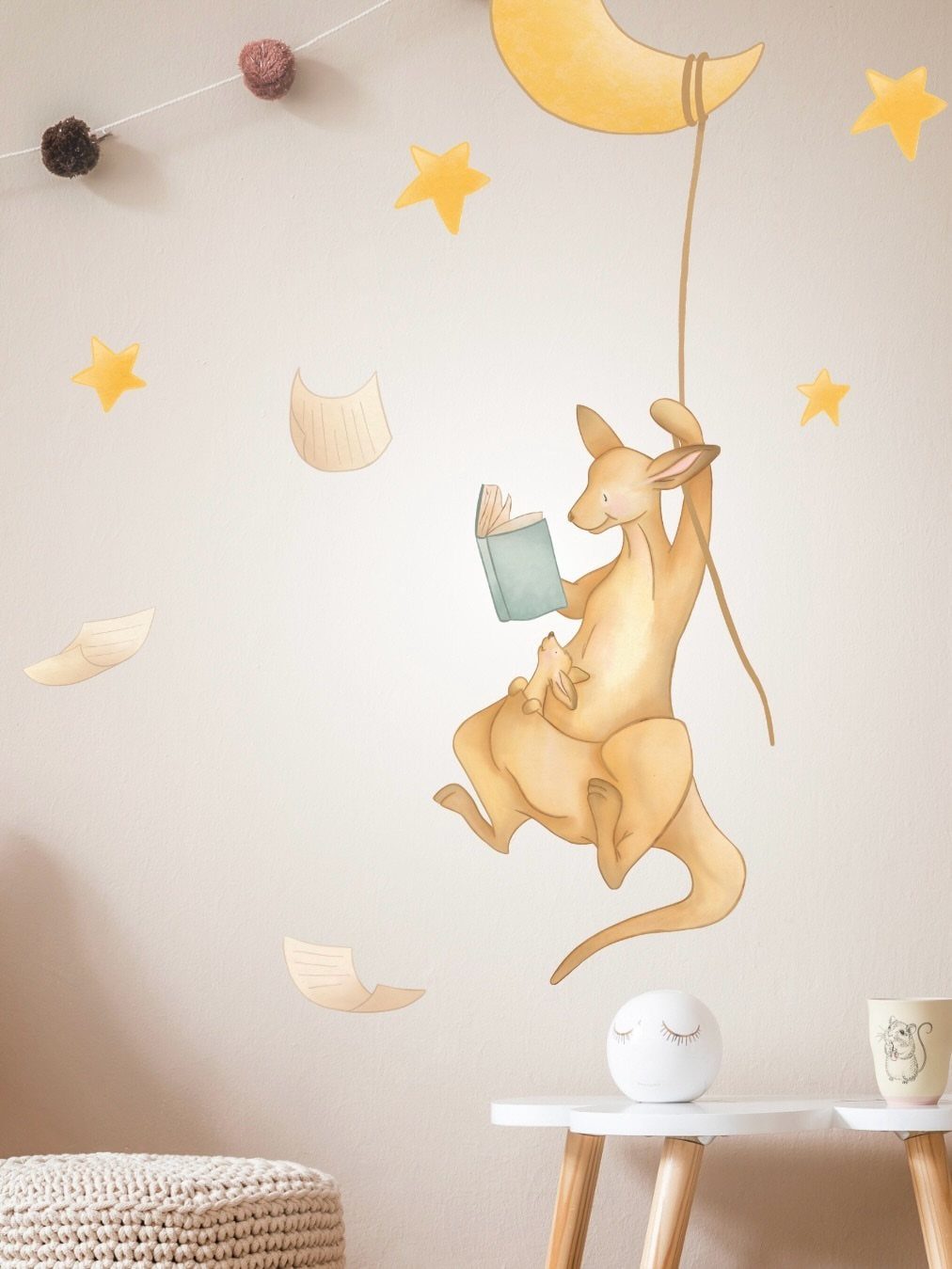Kangaroo reading a book while hanging from a crescent moon on a nursery wall